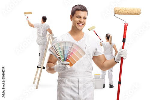 Fototapeta Naklejka Na Ścianę i Meble -  Painter holding a color swatch and a paint roller with two painters painting behind him