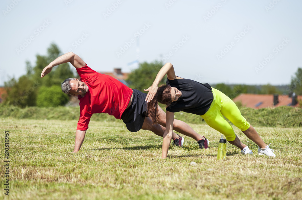 Couple doing side plank exercise on meadow Couple doing side plank exercise on meadow