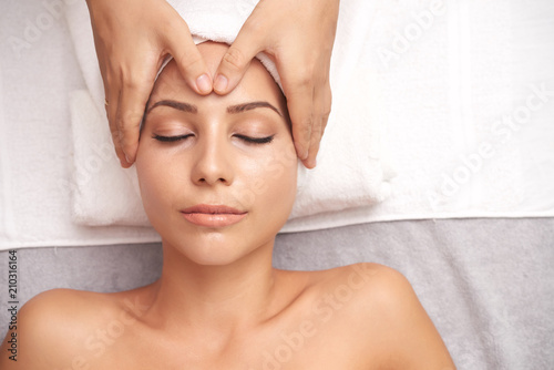 Relaxed young woman lying on white towel during procedure of spa massage with calming effect