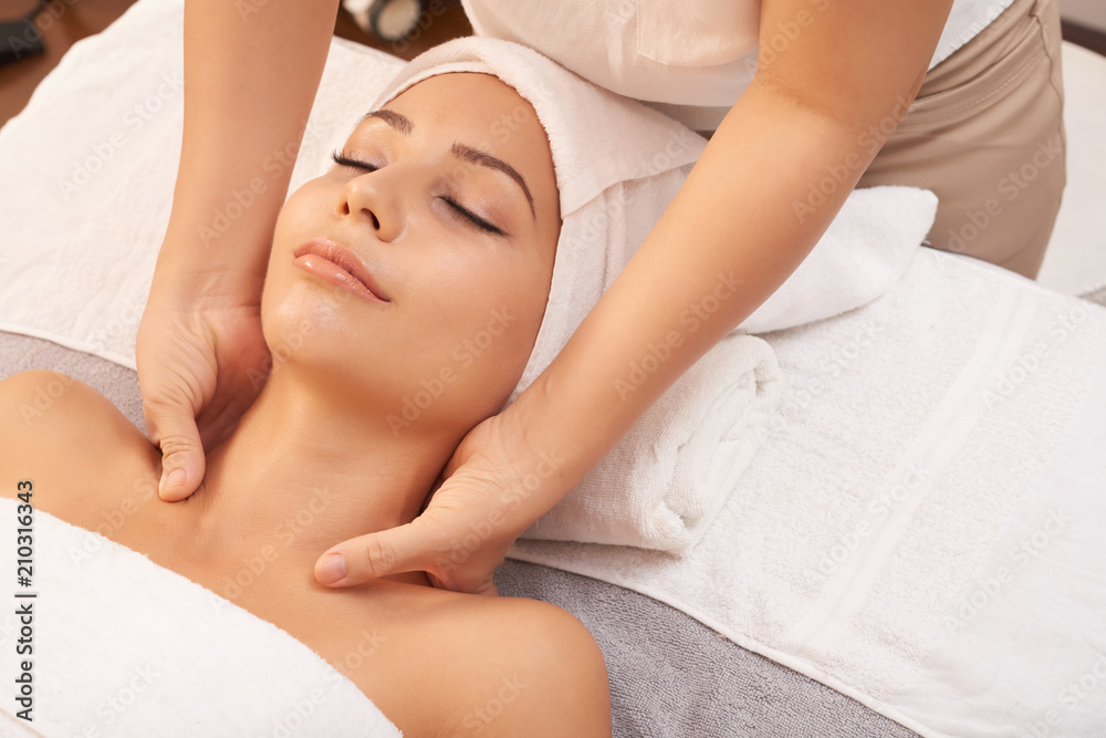 Young female lying on soft towels in spa salon and enjoying relaxing massage of her neck