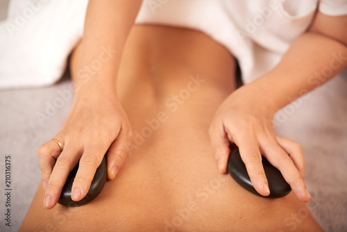 Hands of beautician putting hot spa stones on back of client during beauty procedure
