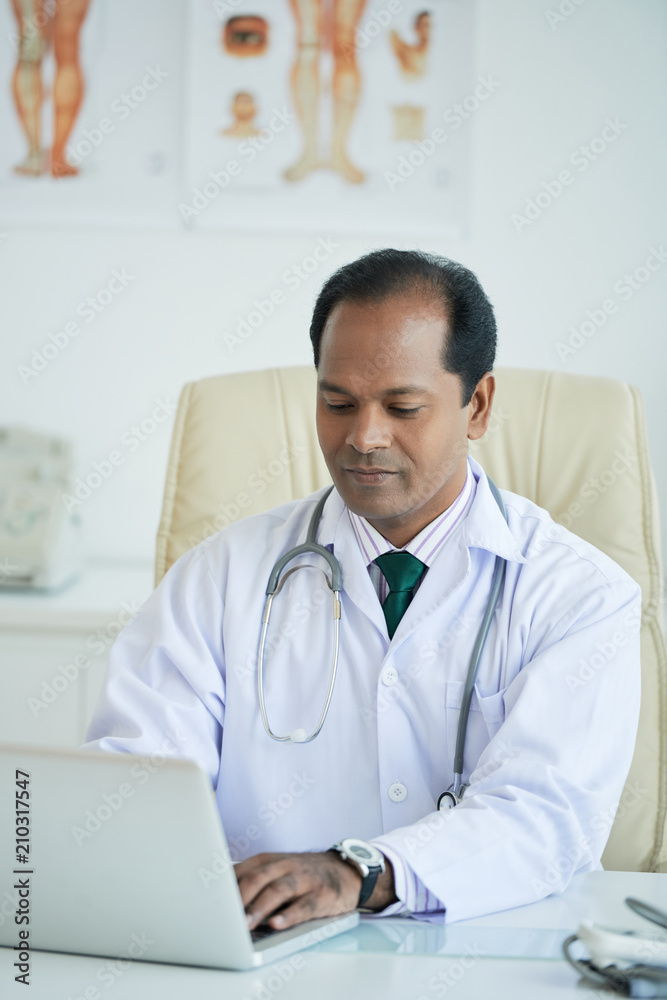 Male doctor sitting at the table and typing on laptop