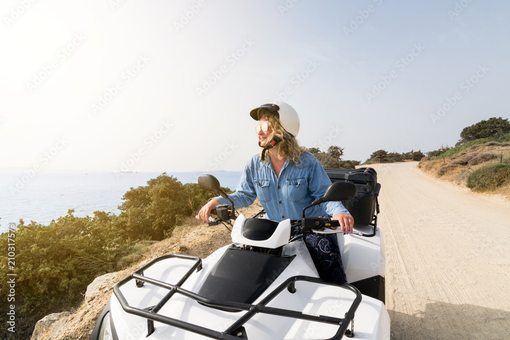 Young woman driving a rental ATV quad bike on seaside road in Naxos island, Greece