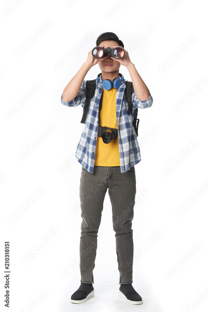Full length portrait of young tourist wearing jeans and checked shirt looking at camera through binoculars while standing against white background Full length portrait of young tourist wearing jeans and checked shirt looking at camera through binoculars while standing against white background