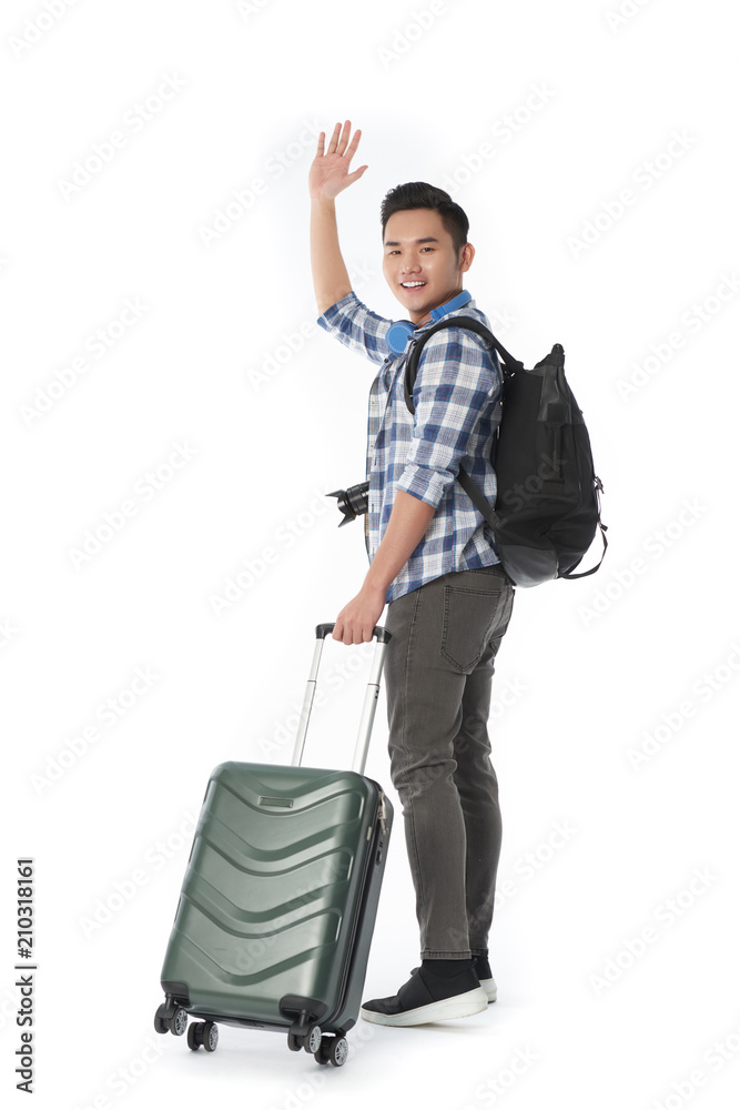 Happy Asian man with suitcase and backpack waving hand to camera while standing against white background, full length portrait Happy Asian man with suitcase and backpack waving hand to camera while standing against white background, full length portrait