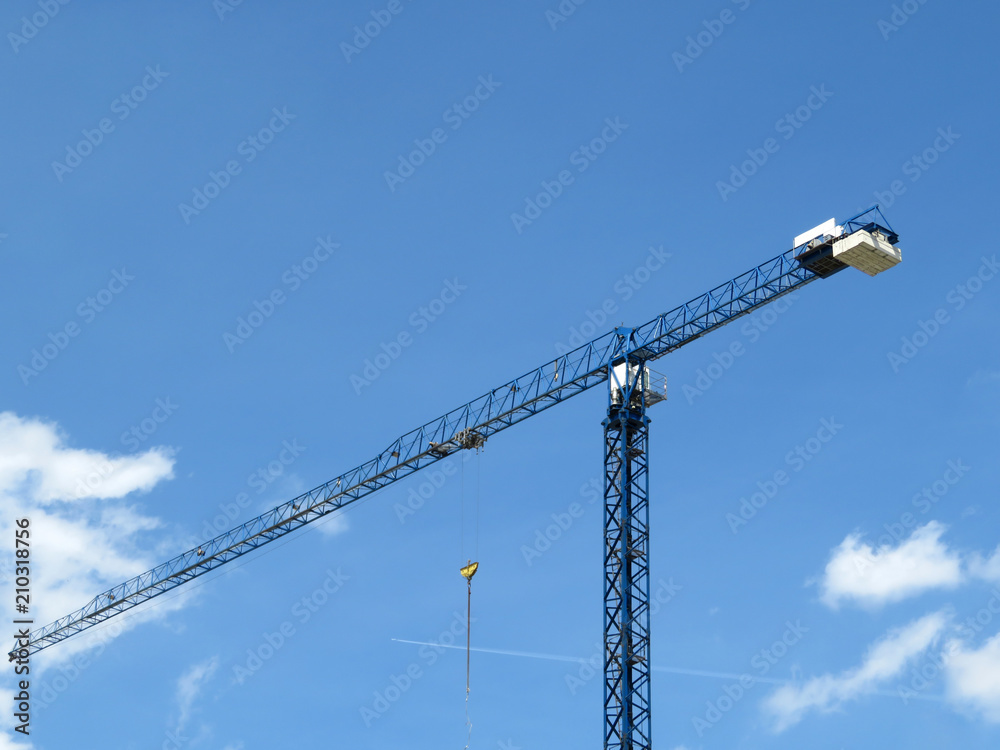 Construction crane against blue sky with clouds and white trace of the plane Construction crane against blue sky with clouds and white trace of the plane