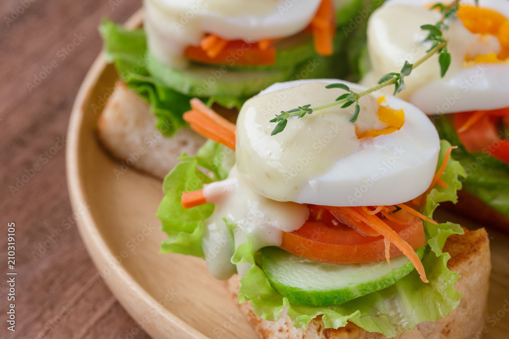 Open faced sandwich with toast and fresh vegetable and boil egg top with salad dressing or mayonnaise on wooden plate. Delicious breakfast for family on wood table. Homemade and healthy food concept.