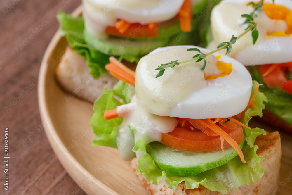 Open faced sandwich with toast and fresh vegetable and boil egg top with salad dressing or mayonnaise on wooden plate. Delicious breakfast for family on wood table. Homemade and healthy food concept. Open faced sandwich with toast and fresh vegetable and boil egg top with salad dressing or mayonnaise on wooden plate. Delicious breakfast for family on wood table. Homemade and healthy food concept.