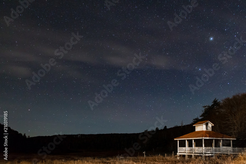 Stary night sky in the mountains with a little white and brown gazebo.