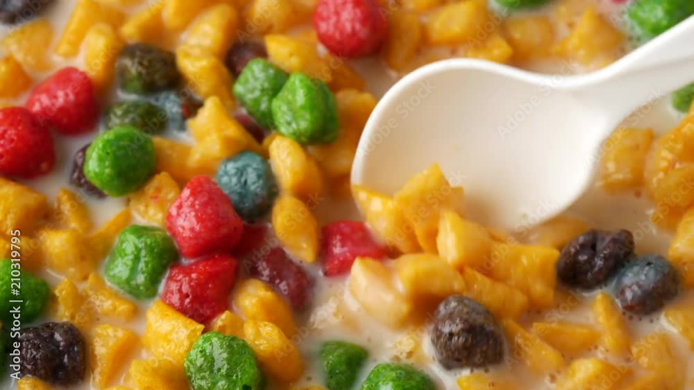 Close video of stirring bright fruit flavor breakfast cereal in milk with a white spoon and taking a spoonful at the end. Close video of stirring bright fruit flavor breakfast cereal in milk with a white spoon and taking a spoonful at the end.