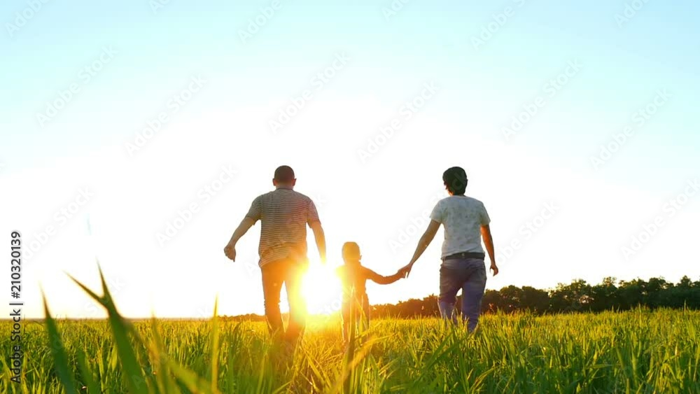 Happy young family with a child running on the green lawn holding hands on a sunset background, in a slow motion Happy young family with a child running on the green lawn holding hands on a sunset background, in a slow motion
