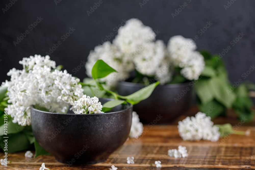 White lilac flowers in ceramic black cups.