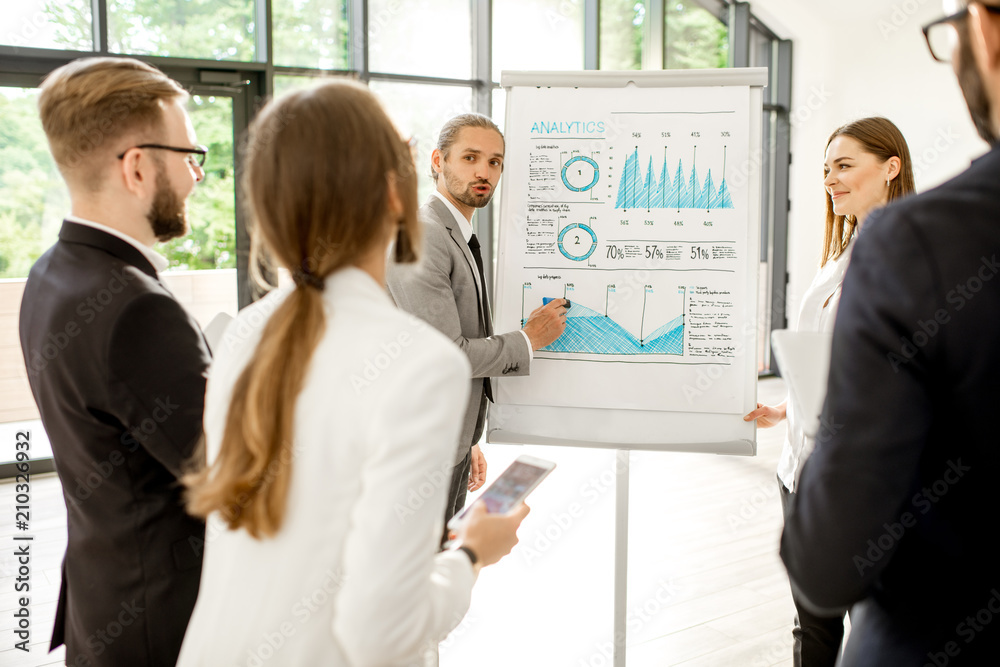 Young speakers reporting with flip chart during the conference standing with business people at the modern office Young speakers reporting with flip chart during the conference standing with business people at the modern office