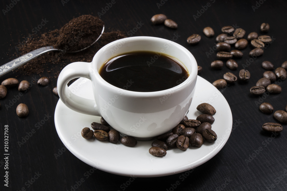 Still life with white cup with delicious coffee and coffee beans on dark background Still life with white cup with delicious coffee and coffee beans on dark background