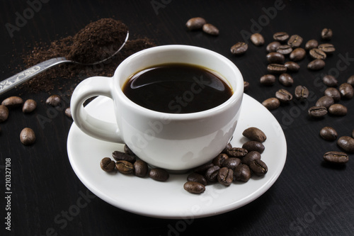 Still life with white cup with delicious coffee and coffee beans on dark background