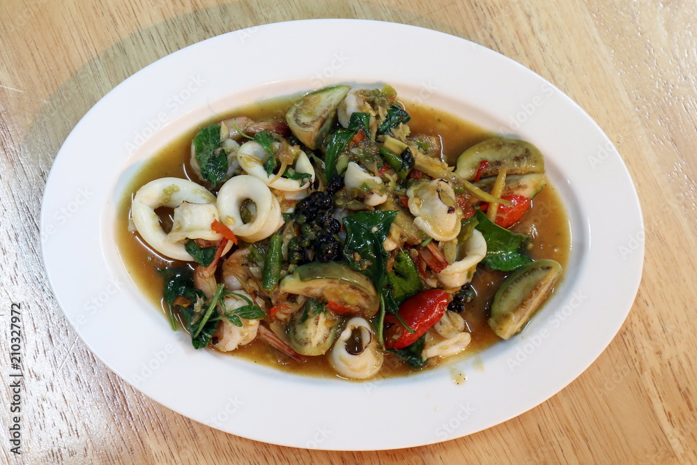 Fried stir sizzle spicy seafood on a white plate - dish at wooden Table, Spicy seafood, Spicy foods, Pad-cha Talay (thai word) Fried stir sizzle spicy seafood on a white plate - dish at wooden Table, Spicy seafood, Spicy foods, Pad-cha Talay (thai word)