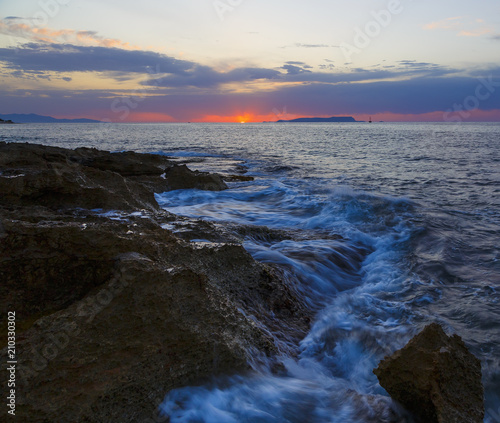 Beautiful cloudscape over the sea, sunrise shot. Waves among the rocks, rocks on horizon. Crete, Greece