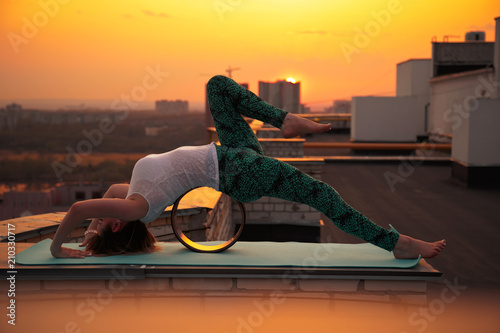 Young caucasian woman doing yoga on a wheel on the roof.