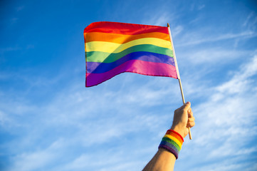 Colorful rainbow gay pride flag being waved in the breeze  by a hand wearing a sweatband