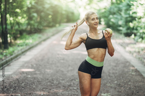 Young Sporty Woman in a Black Sportswear Holds Green Apple in the Openair. Concept of Healthy Lifestyle.