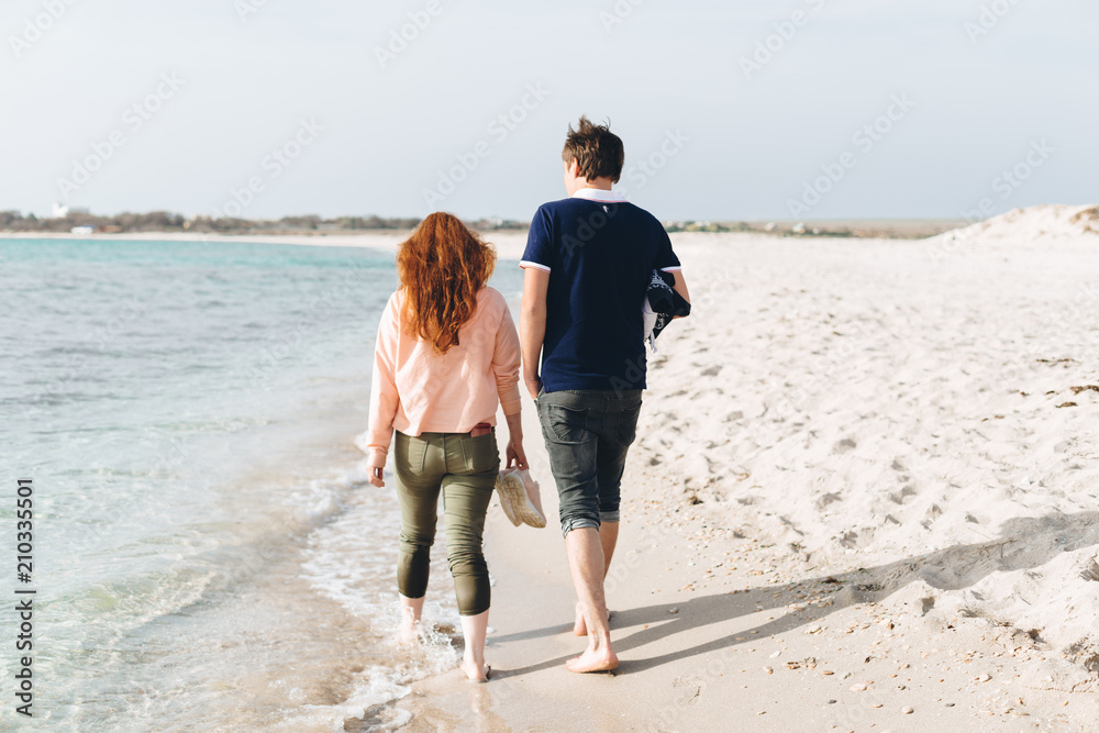A young couple walking barefoot on the sand on an empty beach. A young couple walking barefoot on the sand on an empty beach.