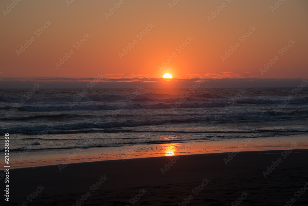 Perfect orange setting sun over a perfect beach of crashing waves