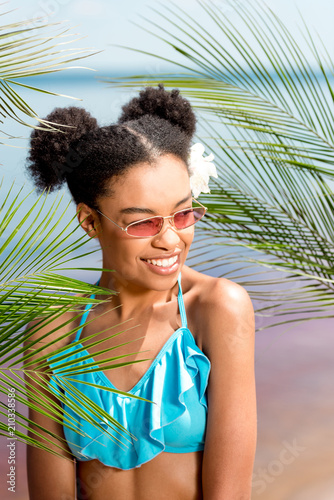 smiling african american woman in sunglasses with flower in hair near palm leaves in front of sea © LIGHTFIELD STUDIOS