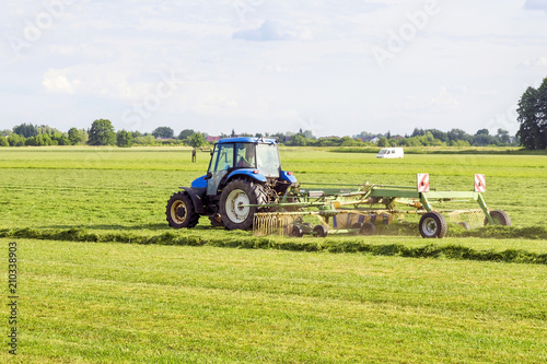 Photos blue tractor rakes hay in the meadow