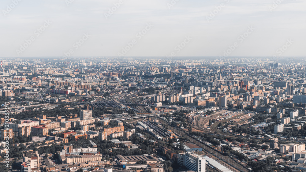 View of sunny megapolis cityscape from high above: huge railroad with multiple tracks, residential districts houses, office buildings and factories, parks and highways, hazy far horizon