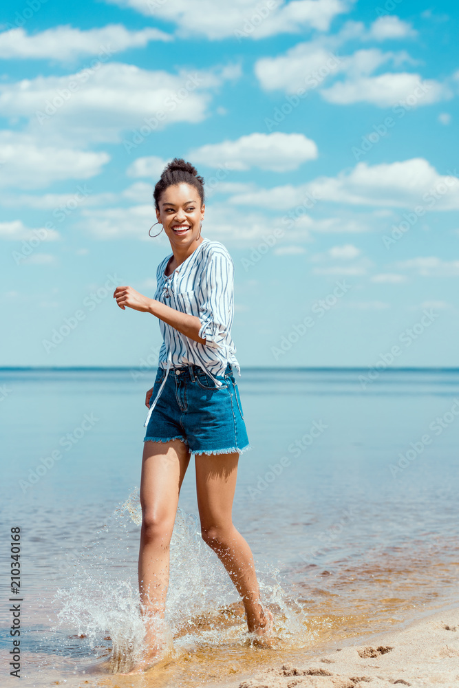 happy african american female tourist walking in sea water near sandy beach happy african american female tourist walking in sea water near sandy beach