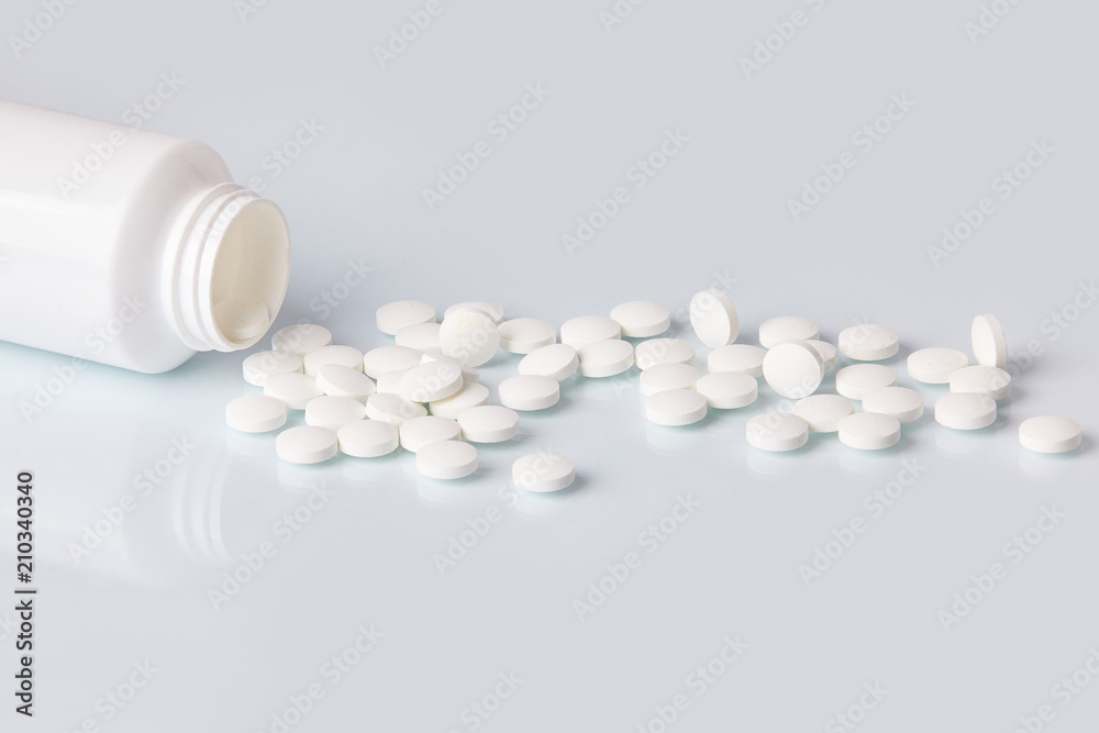 White tablets and pills on white mirror background. Health care concept. Scattered supplements from plastic bottle White tablets and pills on white mirror background. Health care concept. Scattered supplements from plastic bottle