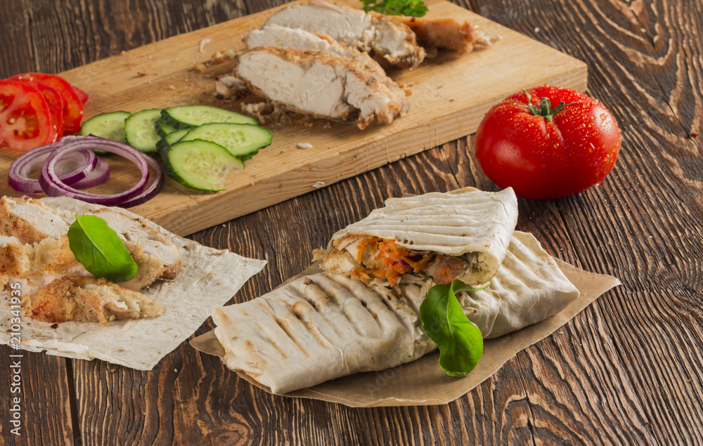 Shaurma, cut in half, meat with vegetables in a bread cake, top view on an old wooden rustic background, on a wooden board with tomato and pepper, copy space Shaurma, cut in half, meat with vegetables in a bread cake, top view on an old wooden rustic background, on a wooden board with tomato and pepper, copy space