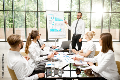 A group of business people strictly dressed in white sitting together during a conference in the spacious office with flip chart on the green background
