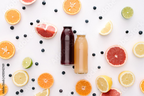 top view of glass bottles of fresh juice with citrus fruits slices on white surface