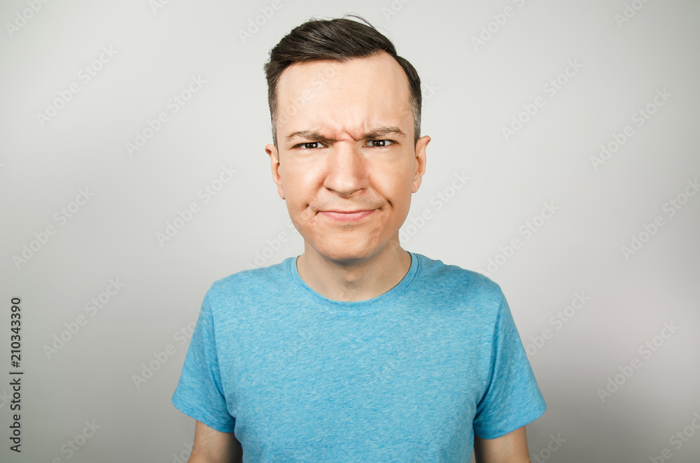 Young unhappy guy with gloomy brows on a light background.