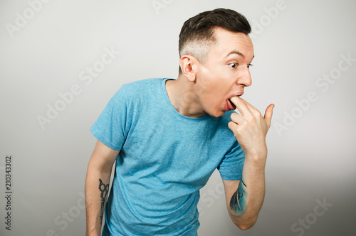 Young guy inserts two fingers in the mouth to induce vomiting, on a light background.