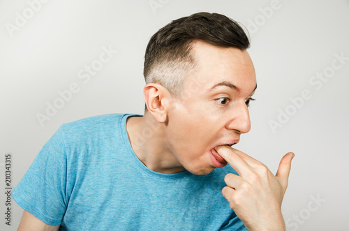 Young guy inserts two fingers in the mouth to induce vomiting, on a light background.