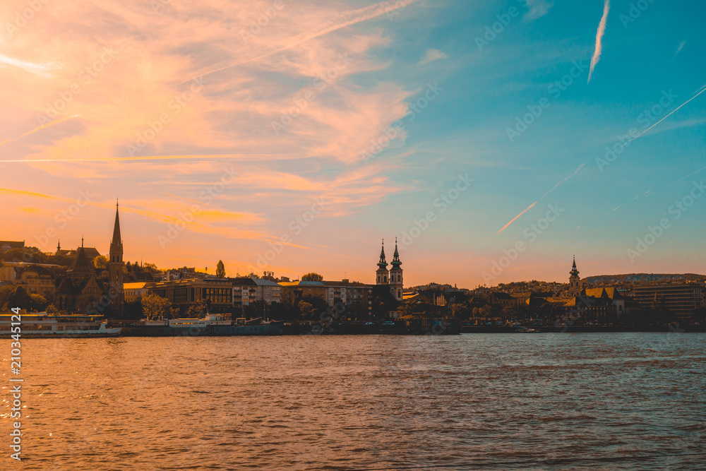 beautiful afternoon scene of danube river at budapest with historical district in the background and orange and blue colored sky