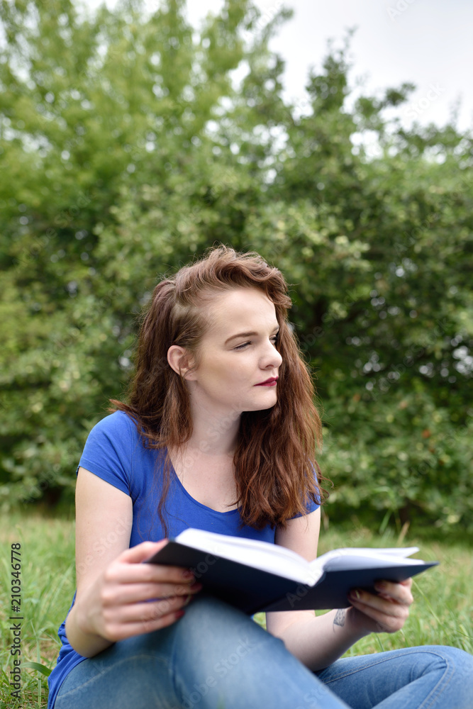 Obraz premium Vertical shot of student reading and dreaming or thinking in a park