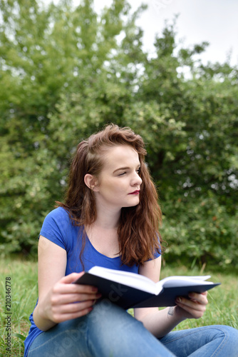 Vertical shot of student reading and dreaming or thinking in a park