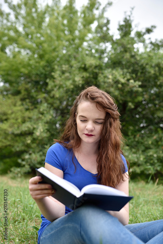 Casual red-head student reading a book in a park