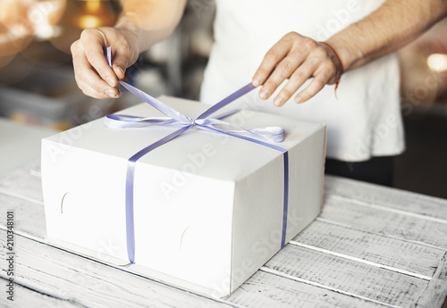Young cook ties violet ribbon on white cake packaging