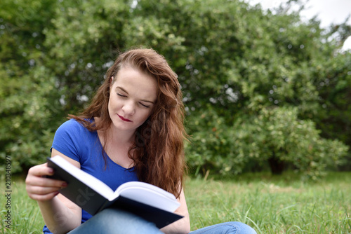 Red-head student reading a book in a park