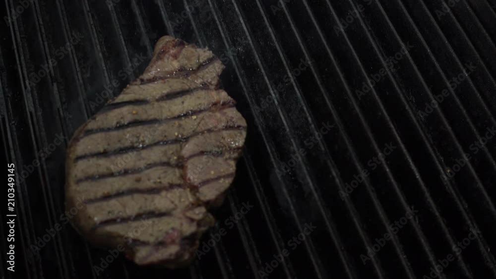 Cooking chief puts uncooked meat piece on hot smoking grill with fire underneath using metal forceps, Close up slow motion. Cooking chief puts uncooked meat piece on hot smoking grill with fire underneath using metal forceps, Close up slow motion.