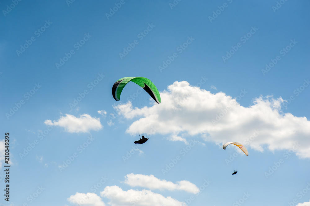 Two paragliders flying in the blue sky against the background of clouds. Paragliding in the sky on a sunny day. Two paragliders flying in the blue sky against the background of clouds. Paragliding in the sky on a sunny day.