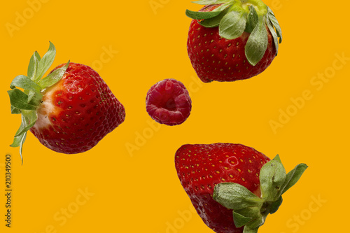 Fototapeta Naklejka Na Ścianę i Meble -  high view of three strawberries with a raspberry in the center with orange background