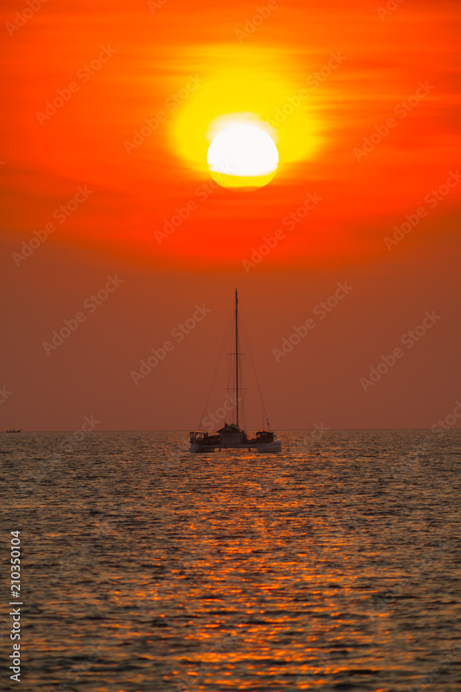 A Boat is floating on the sea under big sunset time at Tropicana located at south of Thailand