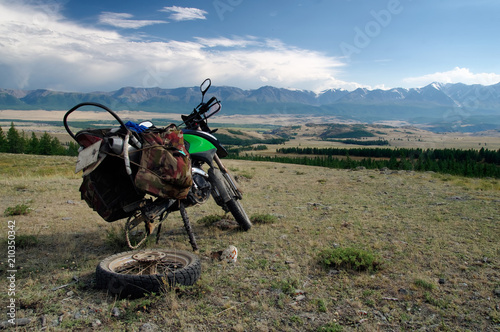 Motorcycle traveler with suitcases repair tire wheel in mountain valley in cloudy weather on the background of gloom fog mountain ranges Altai Mountains Siberia Russia