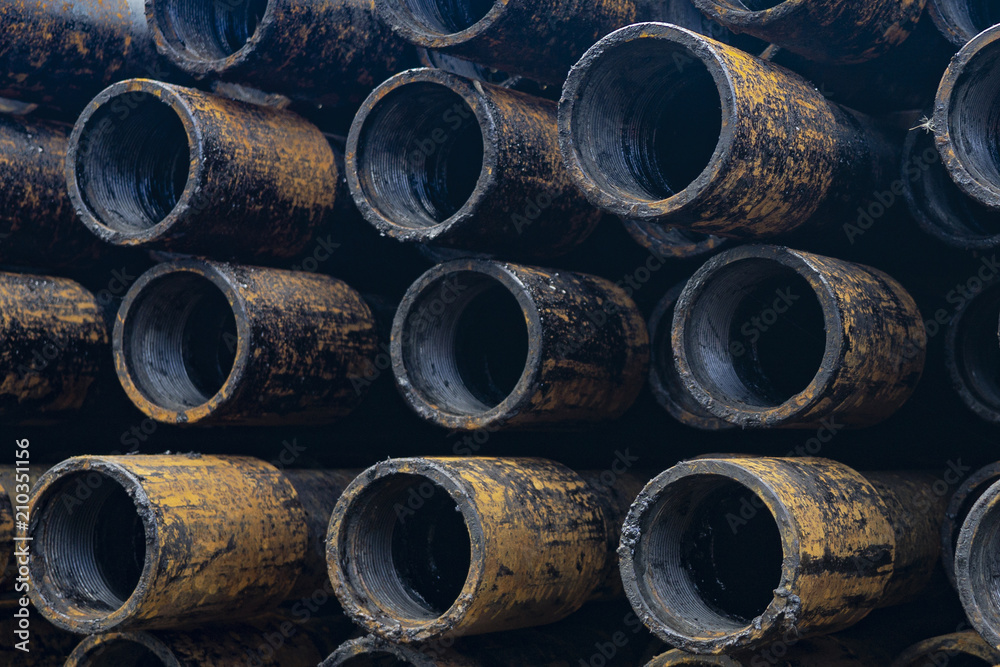 Oil Drill pipe. Rusty drill pipes were drilled in the well section. Downhole drilling rig. Laying the pipe on the deck. View of the shell of drill pipes laid in courtyard of the oil and gas warehouse. Oil Drill pipe. Rusty drill pipes were drilled in the well section. Downhole drilling rig. Laying the pipe on the deck. View of the shell of drill pipes laid in courtyard of the oil and gas warehouse.