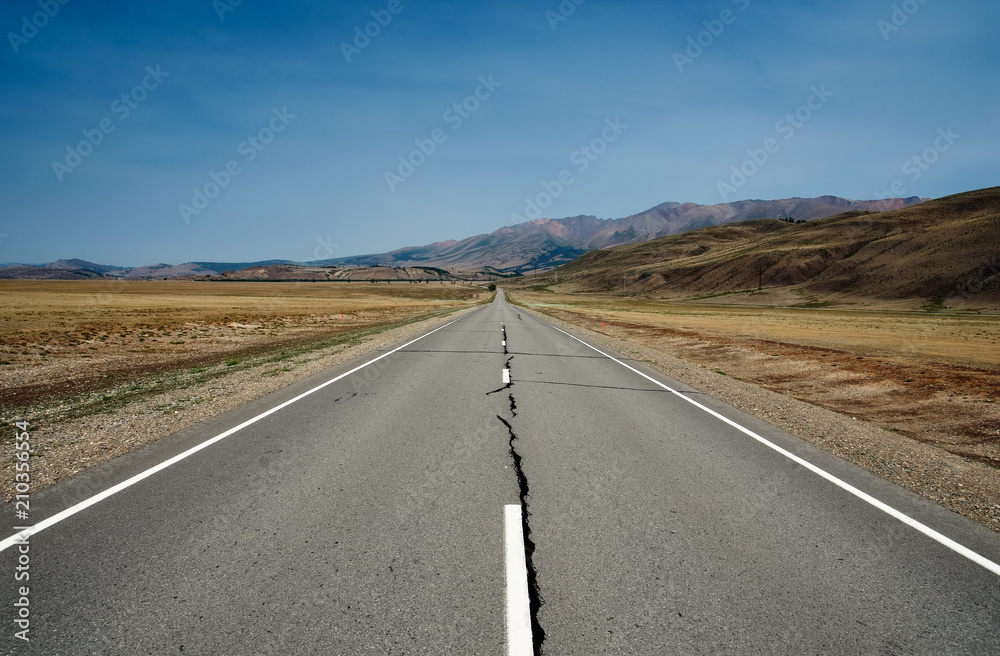 Road asphalt path on a desert wild mountain plateau yellow dry grass at the background of the high ranges under a blue sky Kurai steppe Altai Mountains Siberia, Russia